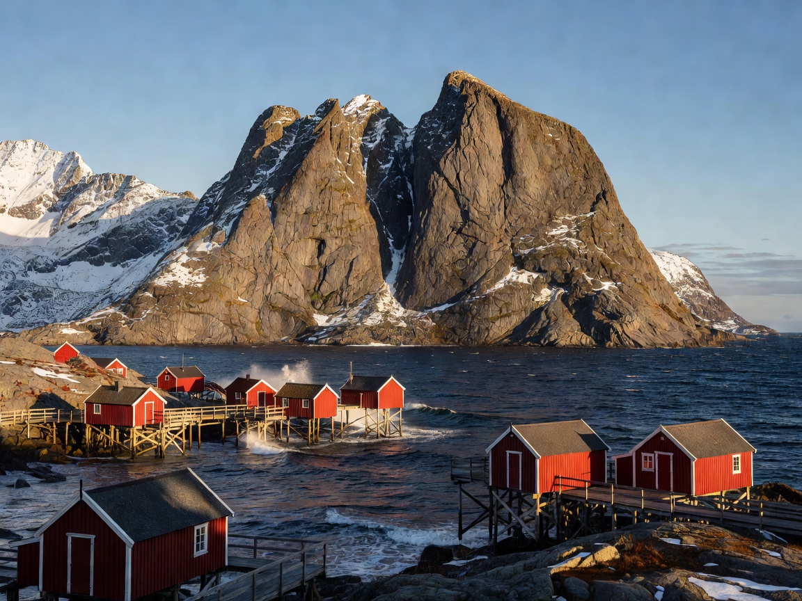 Dramatic mountain peaks rising out of the sea with red fishing cabins in Lofoten, Norway